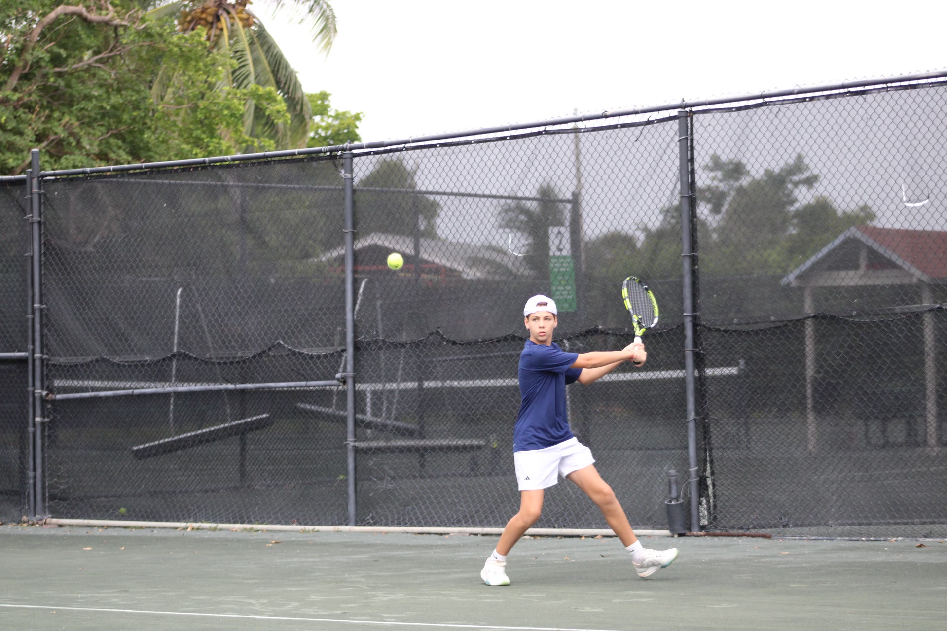 Ari mid-backhand on an outdoor tennis court, tracking the ball